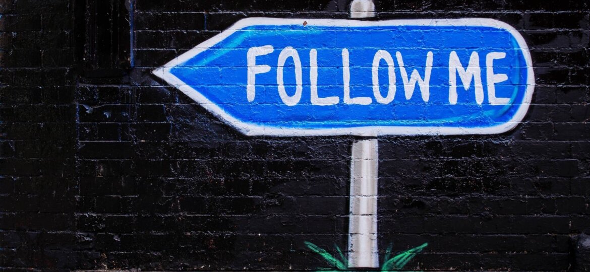 Follow me roadsign on black brick wall